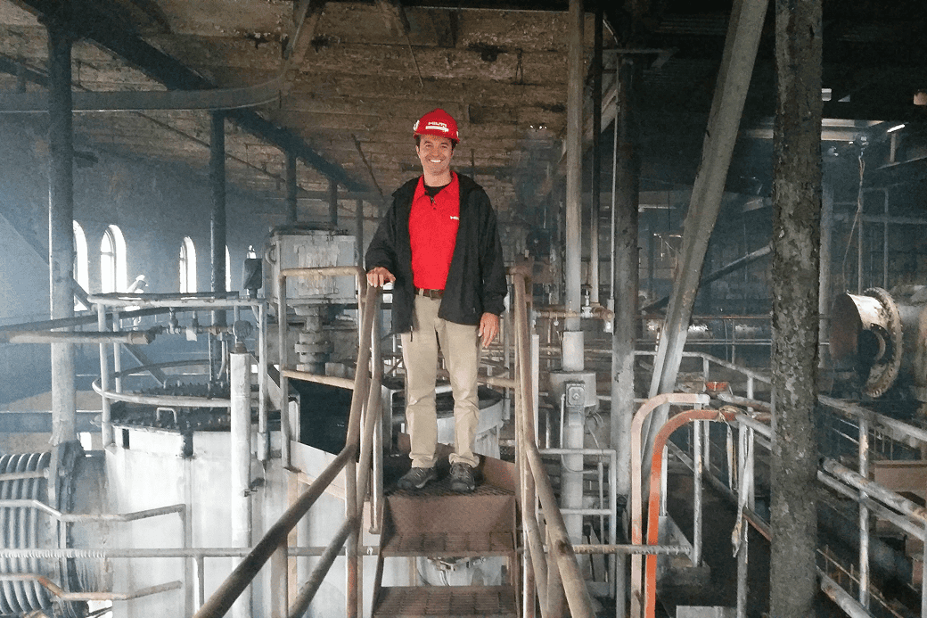 A man standing on a ladder inside a factory, inspecting machinery above him.